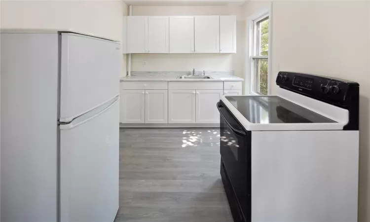 Kitchen with electric range, white cabinetry, a sink, and freestanding refrigerator