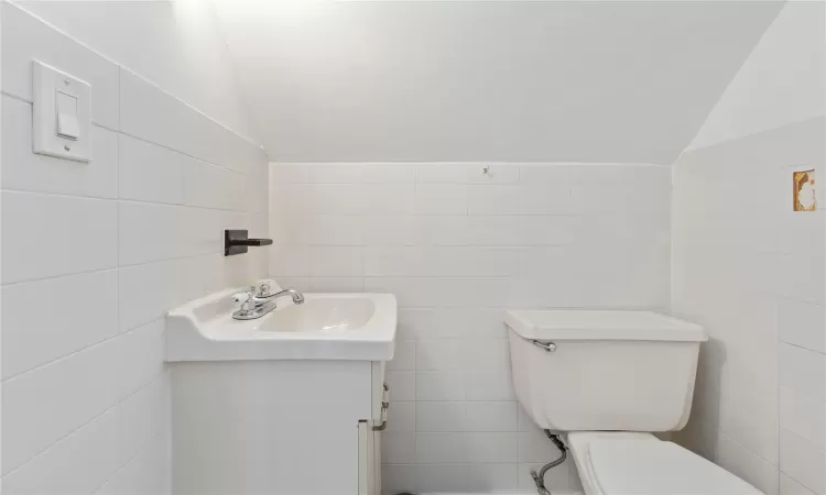 Half bathroom featuring vaulted ceiling, toilet, vanity, and tile walls