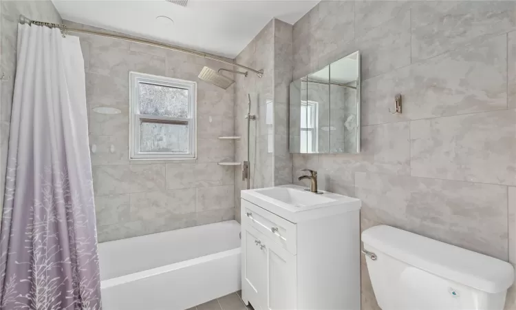 Full bath featuring shower / bath combination with curtain, toilet, tile walls, and vanity