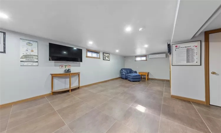 Below grade area with recessed lighting, an AC wall unit, baseboards, and tile patterned floors