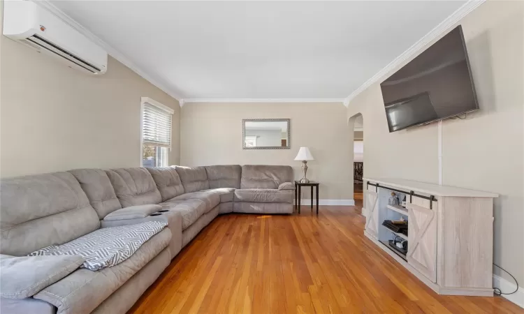 Living area with light wood finished floors, an AC wall unit, ornamental molding, and baseboards