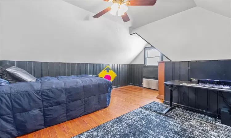 Bedroom featuring radiator heating unit, wooden walls, vaulted ceiling, and wood finished floors