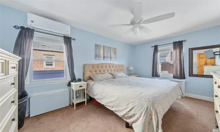 Bedroom with a wall unit AC, ceiling fan, baseboards, and light colored carpet