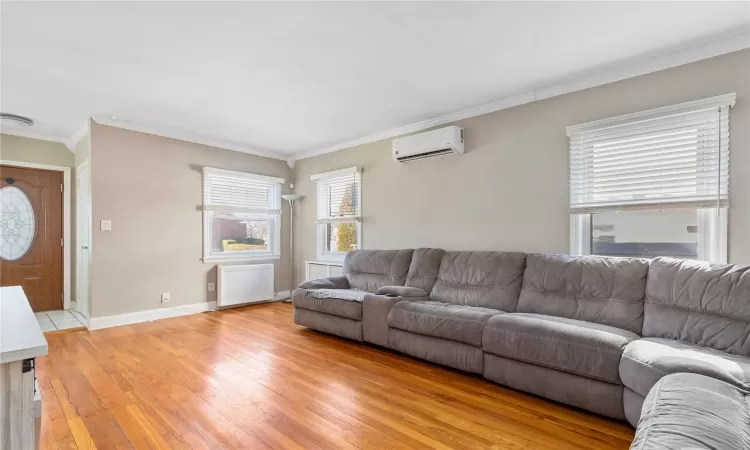 Living area featuring ornamental molding, baseboards, a wall mounted air conditioner, and light wood finished floors