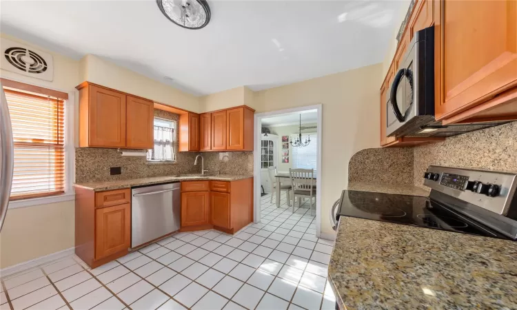 Kitchen with light stone counters, stainless steel appliances, visible vents, brown cabinetry, and a sink