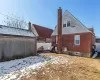 Snow covered rear of property featuring a patio, brick siding, a chimney, and fence