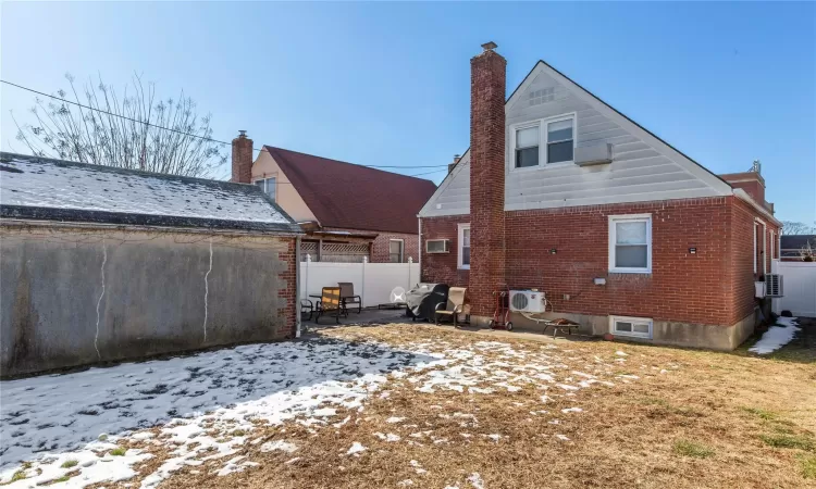 Snow covered rear of property featuring a patio, brick siding, a chimney, and fence