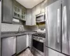 Kitchen with decorative backsplash, glass insert cabinets, appliances with stainless steel finishes, gray cabinets, and a sink