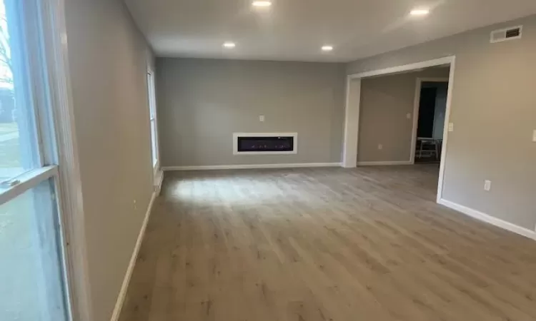 Unfurnished living room featuring recessed lighting, a fireplace, wood finished floors, visible vents, and baseboards