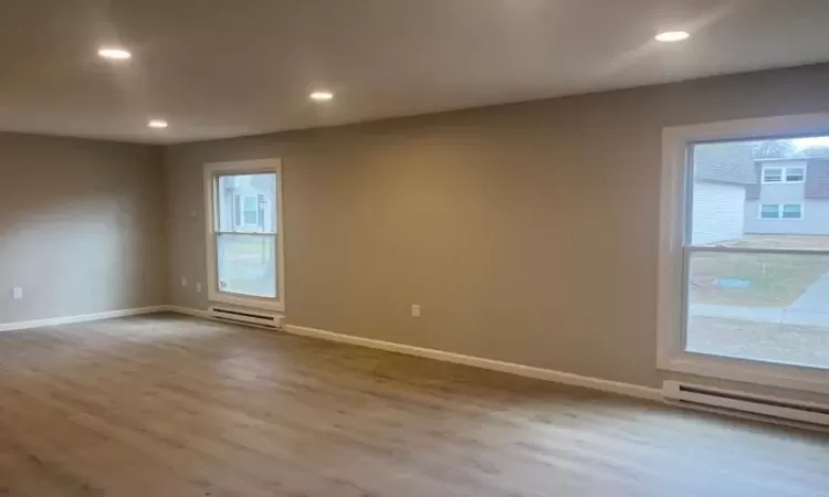 Empty room with a baseboard heating unit, recessed lighting, and wood finished floors