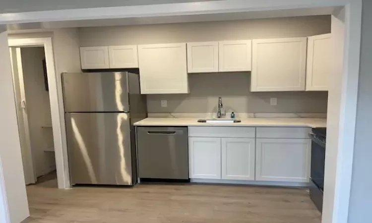 Kitchen featuring light stone counters, appliances with stainless steel finishes, white cabinetry, a sink, and light wood-type flooring