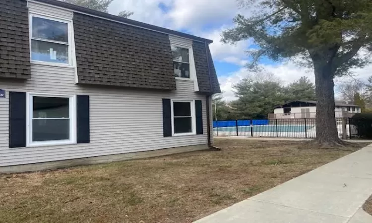 View of home's exterior featuring a fenced in pool near unit, roof with shingles, a yard, mansard roof, and fence