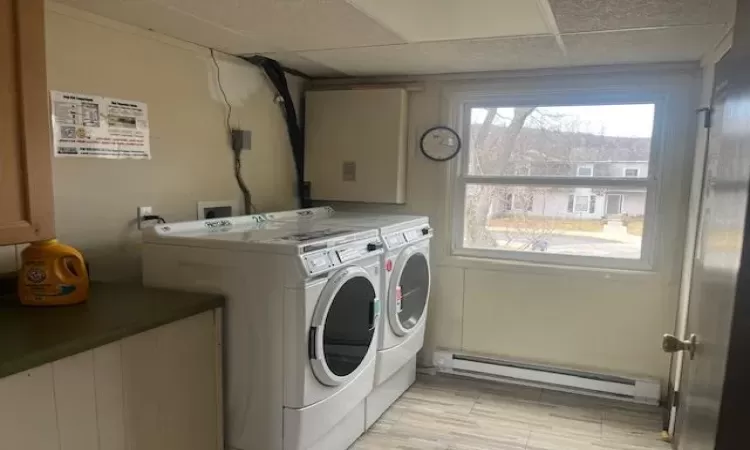 Washroom with light wood-type flooring, cabinet space, washing machine and clothes dryer, and baseboard heating