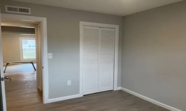 Unfurnished bedroom with a closet, wood finished floors, visible vents, and baseboards