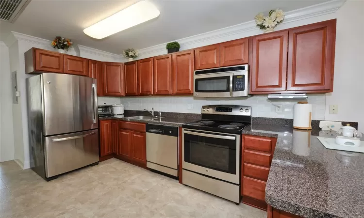 Kitchen with dark countertops, visible vents, appliances with stainless steel finishes, a sink, and a peninsula