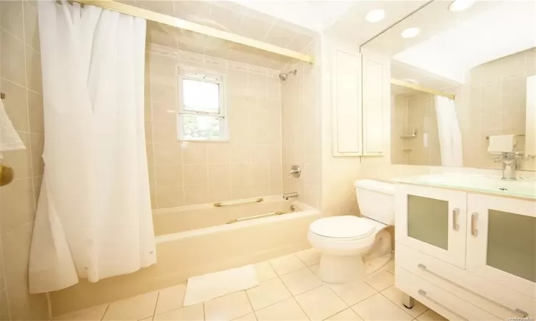 Bathroom featuring toilet, shower / tub combo with curtain, tile patterned flooring, vanity, and tile walls