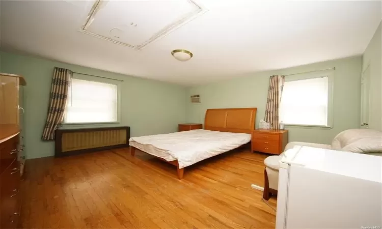 Bedroom with attic access, radiator, a wall mounted air conditioner, and light wood-style flooring