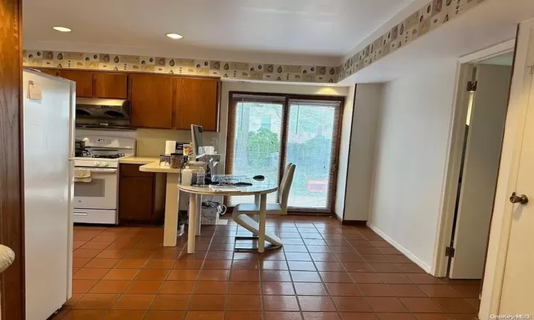 Kitchen with brown cabinets, light countertops, tile patterned flooring, white appliances, and baseboards