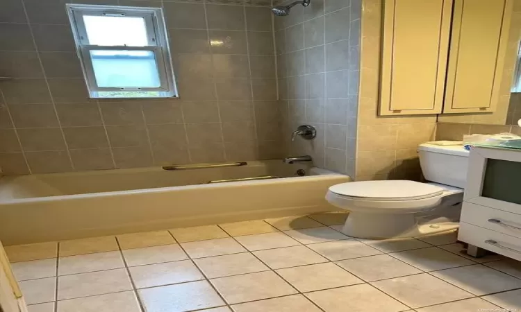 Bathroom featuring bathing tub / shower combination, toilet, tile patterned floors, vanity, and tile walls