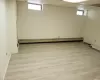 Basement with a healthy amount of sunlight, light wood-style floors, a baseboard radiator, and a drop ceiling