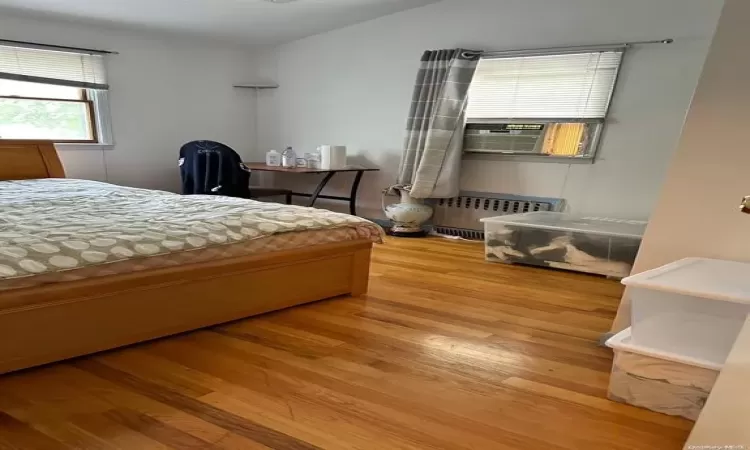 Bedroom featuring cooling unit, radiator, vaulted ceiling, and wood finished floors