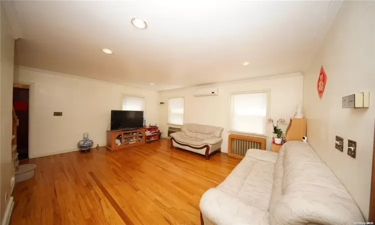 Living area featuring crown molding, recessed lighting, radiator heating unit, an AC wall unit, and light wood-type flooring