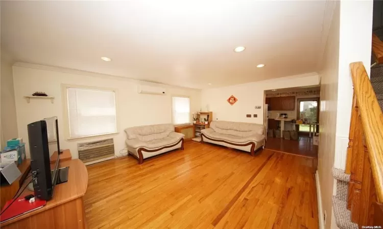 Living area with a wall unit AC, crown molding, and light wood-style flooring