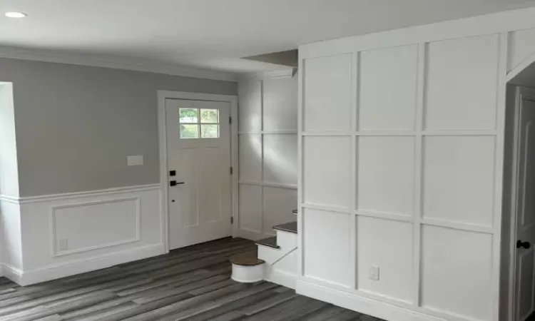 Entrance foyer with recessed lighting, a decorative wall, ornamental molding, dark wood-type flooring, and wainscoting