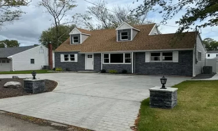 New england style home with central air condition unit, a shingled roof, curved driveway, and a front yard