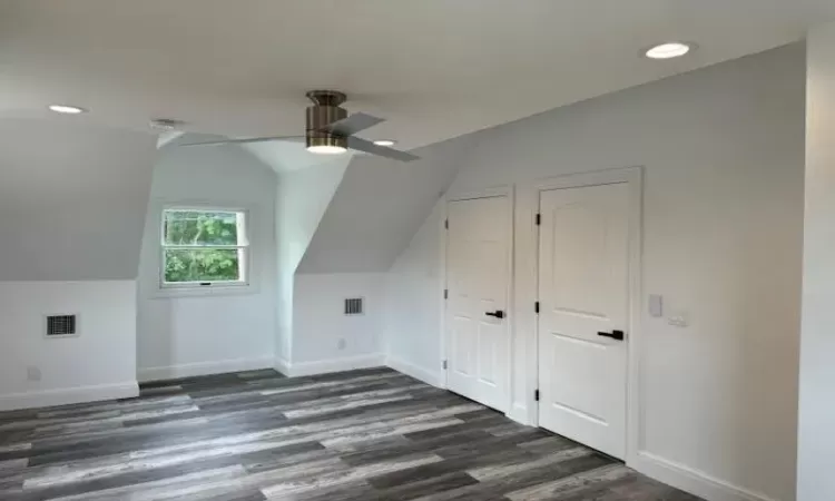 Bonus room with dark wood-style floors, lofted ceiling, visible vents, and baseboards