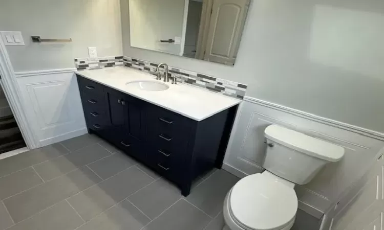 Bathroom with a wainscoted wall, vanity, toilet, and tile patterned floors