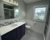 Full bath with tile patterned flooring, toilet, vanity, tiled shower, and wainscoting