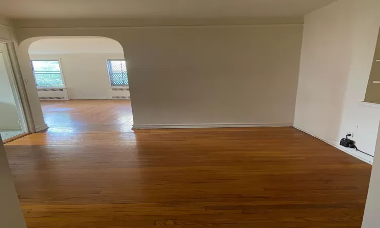 Empty room with arched walkways, wood finished floors, and radiator