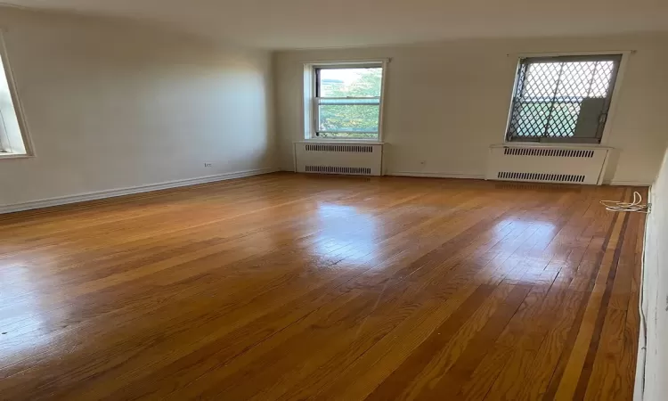 Unfurnished room with baseboards, wood-type flooring, and radiator