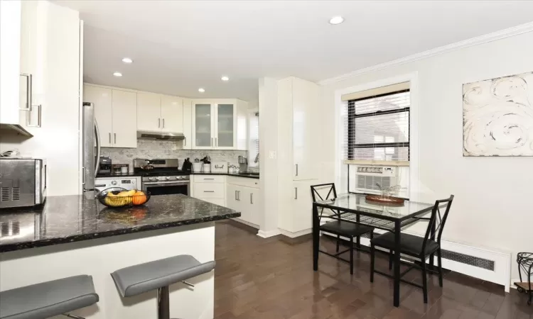 Kitchen with appliances with stainless steel finishes, crown molding, under cabinet range hood, and decorative backsplash