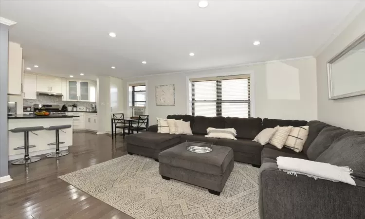 Living room with dark wood-style floors, ornamental molding, and recessed lighting