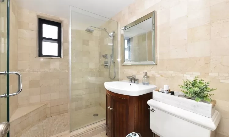 Full bath featuring a stall shower, tasteful backsplash, toilet, vanity, and tile walls