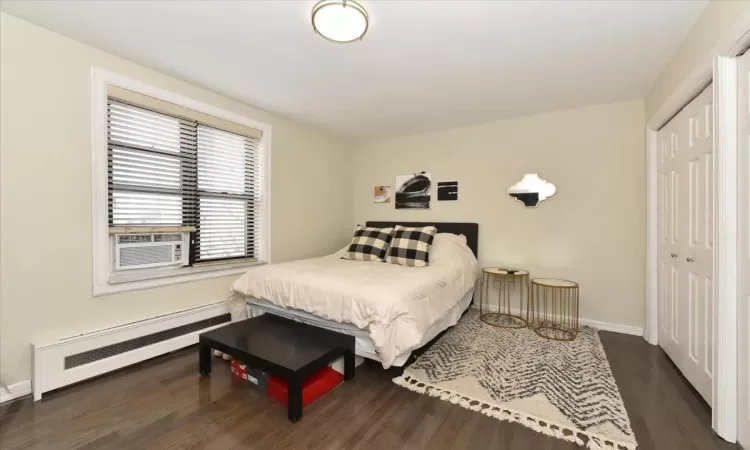 Bedroom with baseboards, radiator heating unit, dark wood-type flooring, cooling unit, and a closet