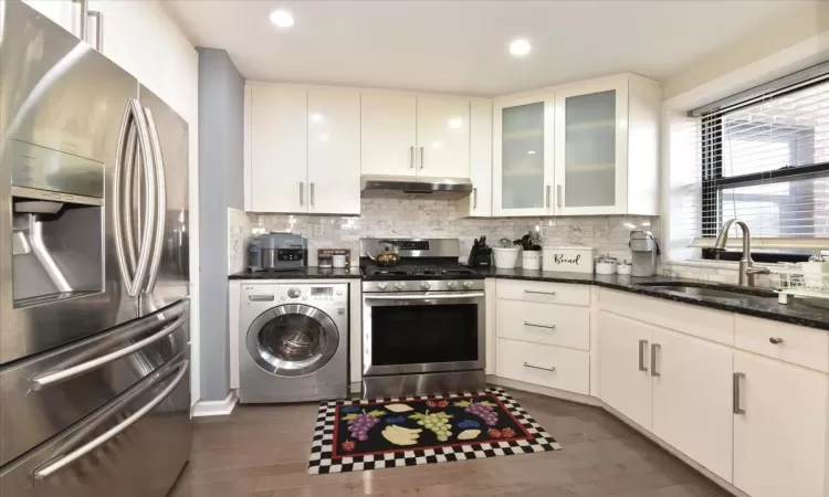 Kitchen with under cabinet range hood, stainless steel appliances, a sink, decorative backsplash, and washer / dryer