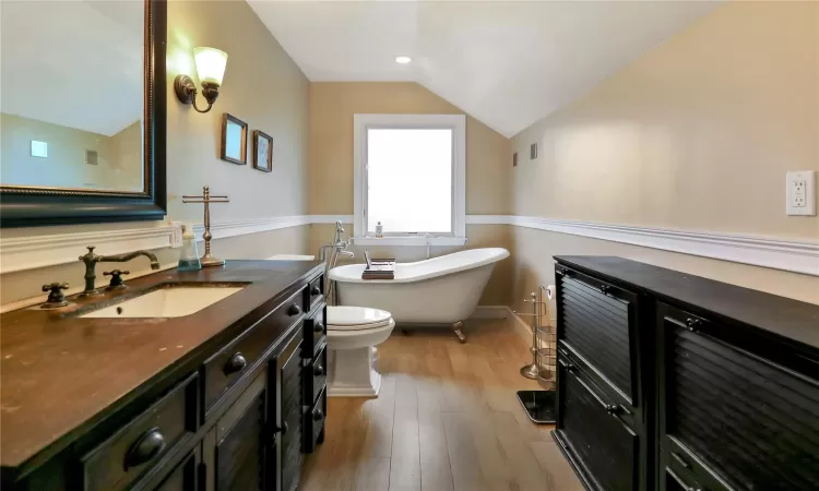 Full bath on the second floor featuring lofted ceiling, toilet, vanity, wood finished floors, and a freestanding tub