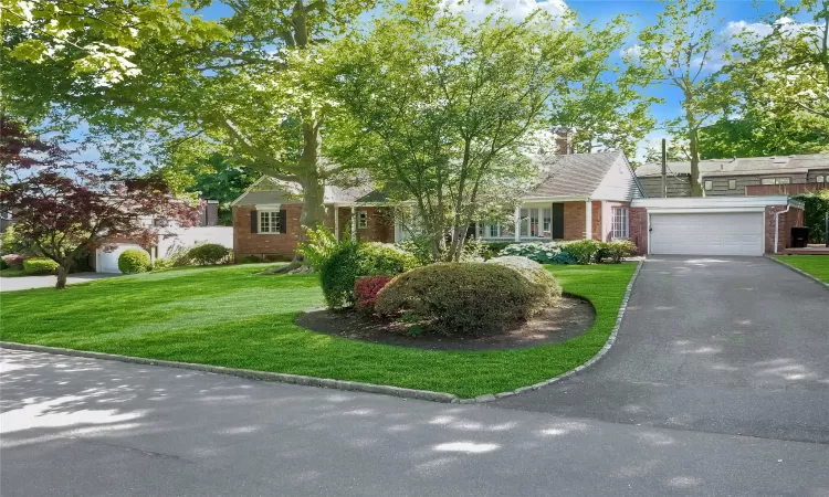 View of front of property featuring aphalt driveway, a chimney, a front lawn, and brick siding