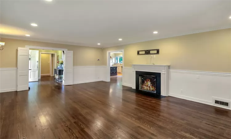 Unfurnished living room with dark wood finished floors, ornamental molding, a fireplace with flush hearth, and visible vents