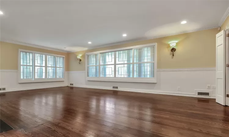 Unfurnished living room with dark wood-style floors, visible vents, and ornamental molding