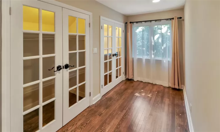 Second floor bedroom with an open doorway featuring french doors, dark wood finished floors, and baseboards