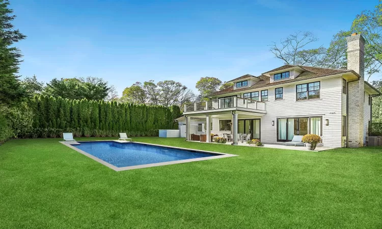 Back of house featuring an outdoor pool, a lawn, and a balcony