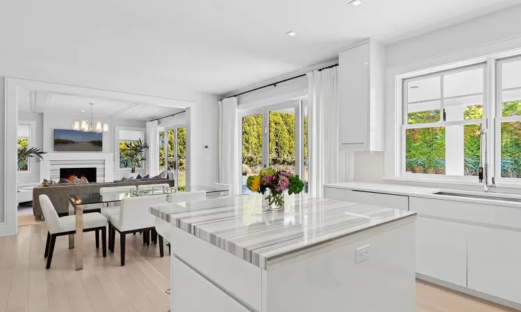 Kitchen with a lit fireplace, a kitchen island, light wood-style flooring, and white cabinets