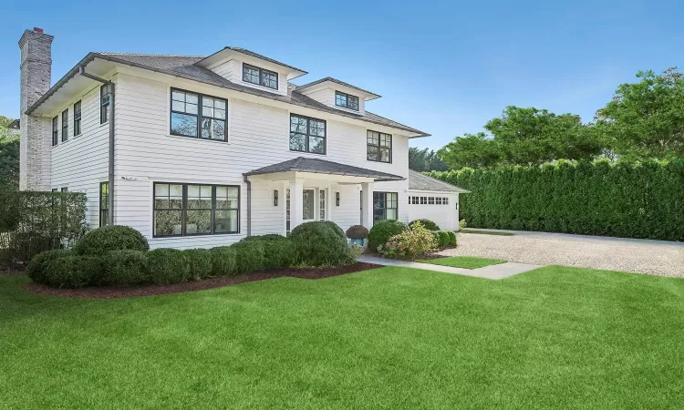 Traditional style home featuring an attached garage, driveway, a chimney, and a front yard