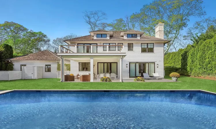 Back of house with an outdoor pool, a lawn, a patio, a balcony, and an outdoor living space