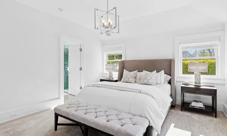 Bedroom featuring vaulted ceiling, light wood finished floors, an inviting chandelier, and baseboards