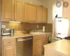 Kitchen featuring light countertops, backsplash, stainless steel dishwasher, light brown cabinetry, and a sink